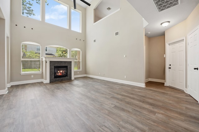 unfurnished living room featuring a towering ceiling, healthy amount of natural light, wood finished floors, and a glass covered fireplace