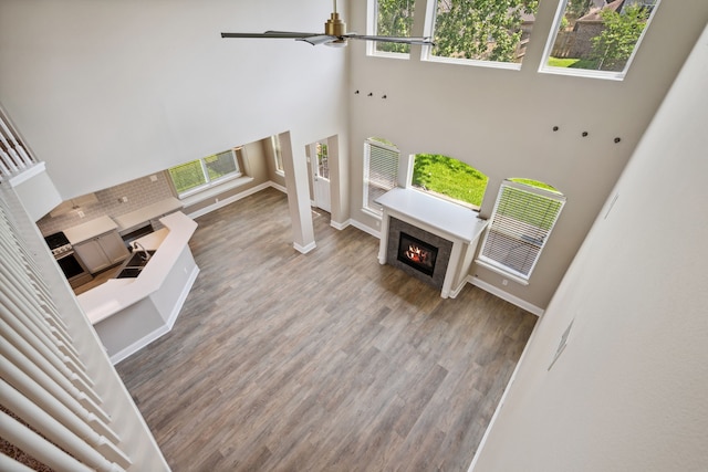 living room with a high ceiling, a glass covered fireplace, ceiling fan, plenty of natural light, and baseboards