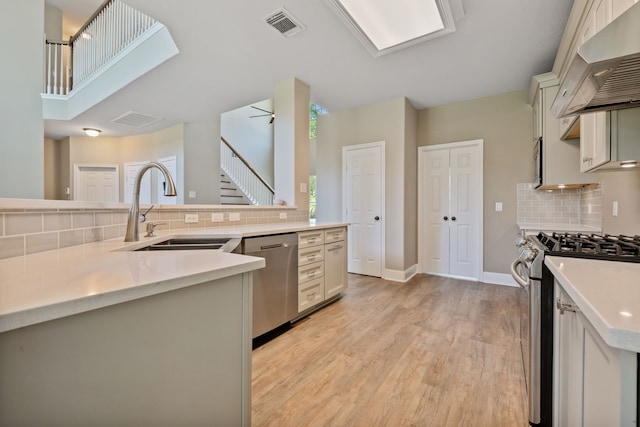 kitchen featuring stainless steel appliances, a sink, exhaust hood, decorative backsplash, and light countertops