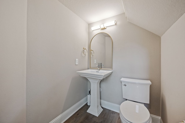 half bath featuring toilet, wood finished floors, baseboards, lofted ceiling, and a textured ceiling