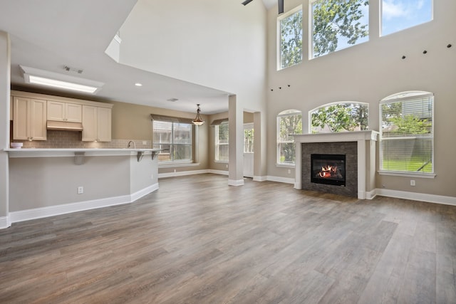 unfurnished living room featuring wood finished floors, a glass covered fireplace, baseboards, and a towering ceiling