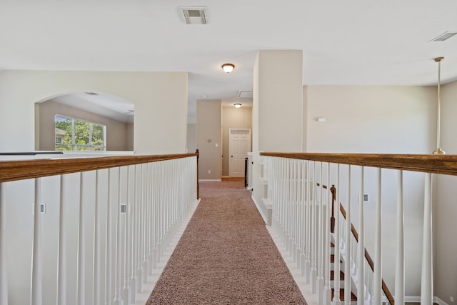 hallway with light carpet, arched walkways, and baseboards