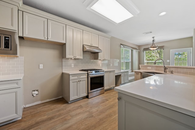 kitchen featuring appliances with stainless steel finishes, a sink, decorative backsplash, light countertops, and light wood-type flooring