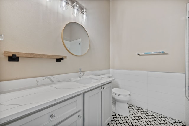 bathroom featuring toilet, vanity, a wainscoted wall, tile walls, and tile patterned floors
