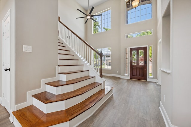 foyer with a towering ceiling, wood finished floors, stairs, baseboards, and a ceiling fan
