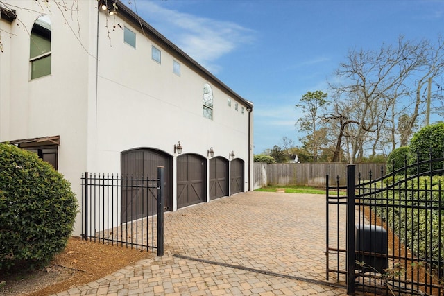 view of side of home featuring decorative driveway, an attached garage, a gate, fence, and stucco siding