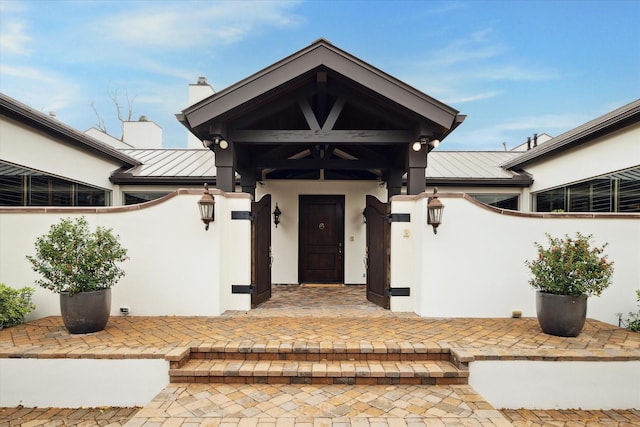 view of front facade with a standing seam roof, stucco siding, metal roof, and fence