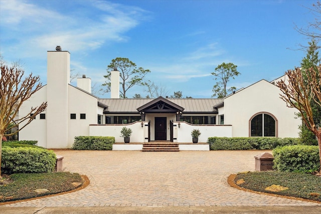 view of front of property with stucco siding, a chimney, and metal roof