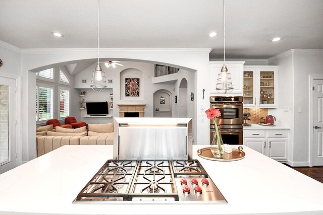 kitchen with appliances with stainless steel finishes, arched walkways, ornamental molding, white cabinetry, and a fireplace