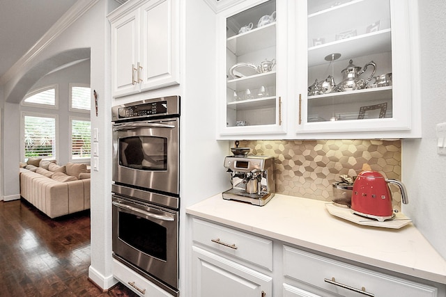 kitchen with stainless steel double oven, glass insert cabinets, white cabinets, dark wood finished floors, and backsplash
