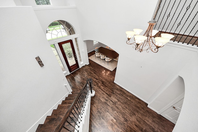 foyer featuring arched walkways, a high ceiling, a chandelier, wood finished floors, and stairs