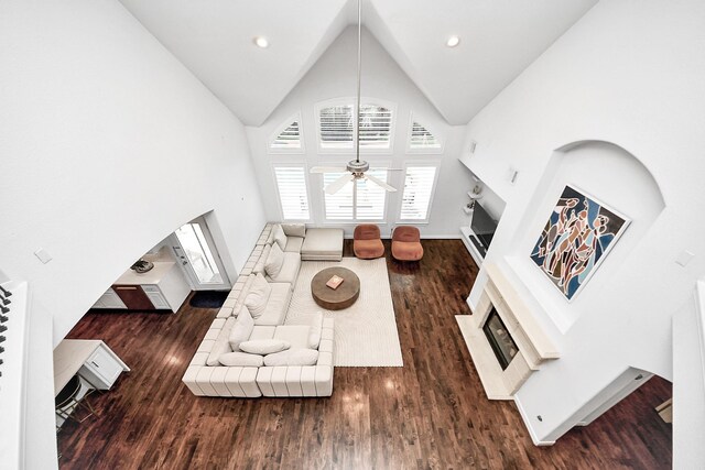 living area with wood finished floors, a glass covered fireplace, high vaulted ceiling, ceiling fan, and arched walkways