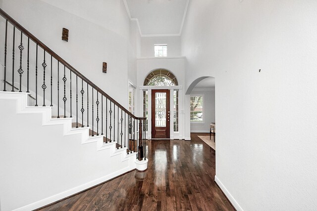 foyer featuring arched walkways, baseboards, wood finished floors, stairway, and a high ceiling