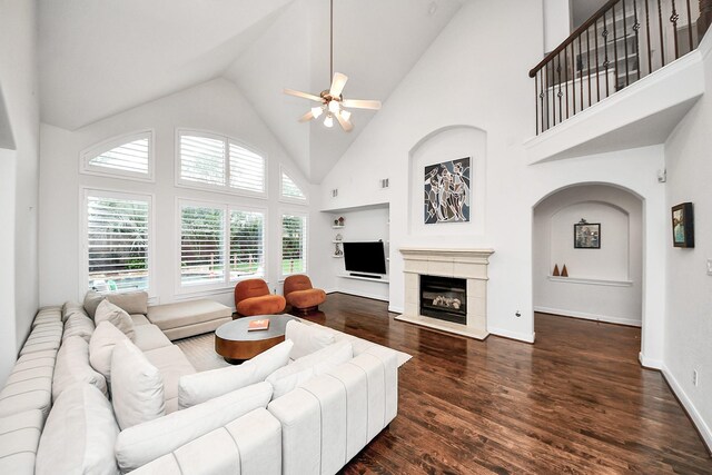 living room featuring a ceiling fan, wood finished floors, high vaulted ceiling, a glass covered fireplace, and baseboards