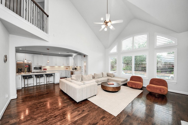 living area featuring high vaulted ceiling, dark wood-style floors, arched walkways, a ceiling fan, and baseboards