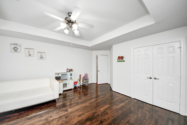 sitting room with a tray ceiling, wood finished floors, and ceiling fan