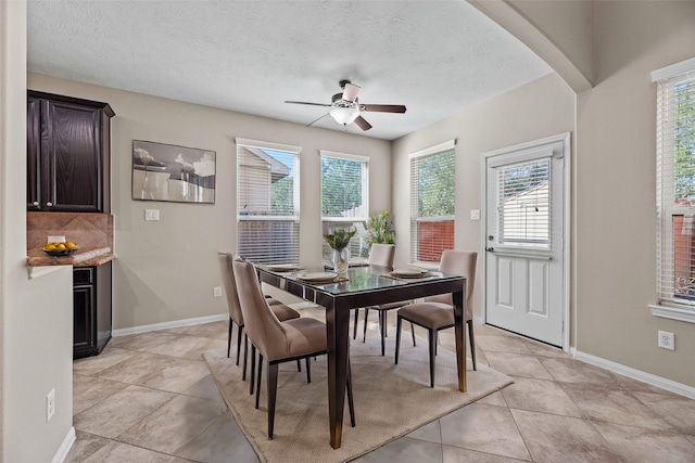 dining area with ceiling fan, baseboards, light tile patterned flooring, a textured ceiling, and arched walkways