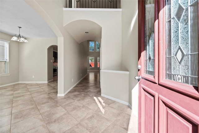foyer entrance featuring arched walkways, a chandelier, light tile patterned floors, and baseboards