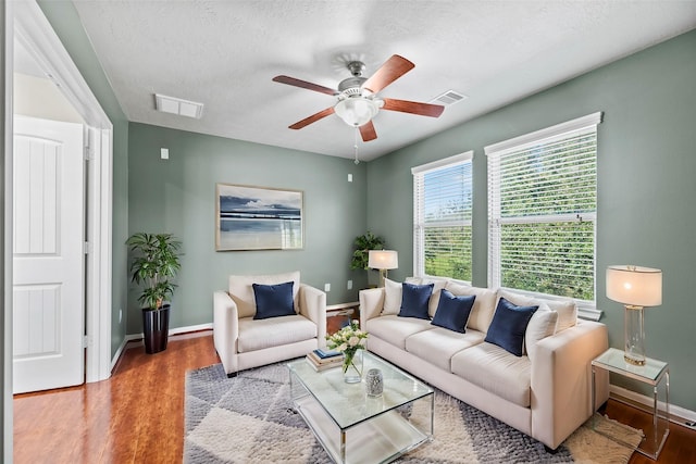living room featuring a ceiling fan, wood finished floors, baseboards, and a textured ceiling