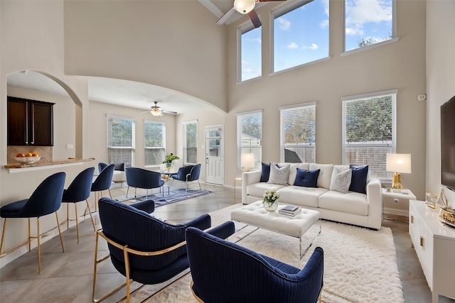 living room with ceiling fan, a towering ceiling, plenty of natural light, arched walkways, and baseboards