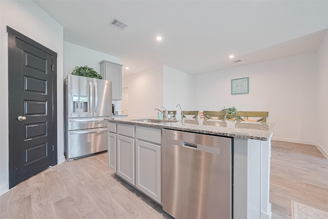 31707 Whittis Hill Way, Fulshear, TX 77441 - kitchen with appliances with stainless steel finishes, light wood-style floors, a kitchen island with sink, light stone counters, and recessed lighting