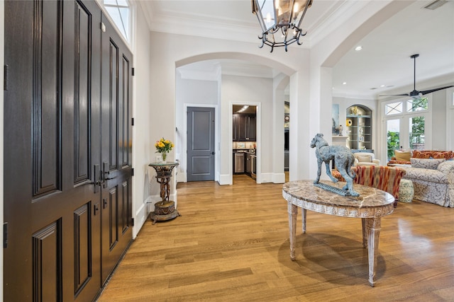 foyer entrance with a ceiling fan, arched walkways, crown molding, light wood-style floors, and recessed lighting