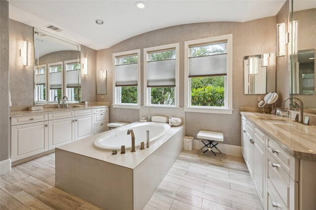 bathroom with two vanities, a bath, lofted ceiling, and baseboards