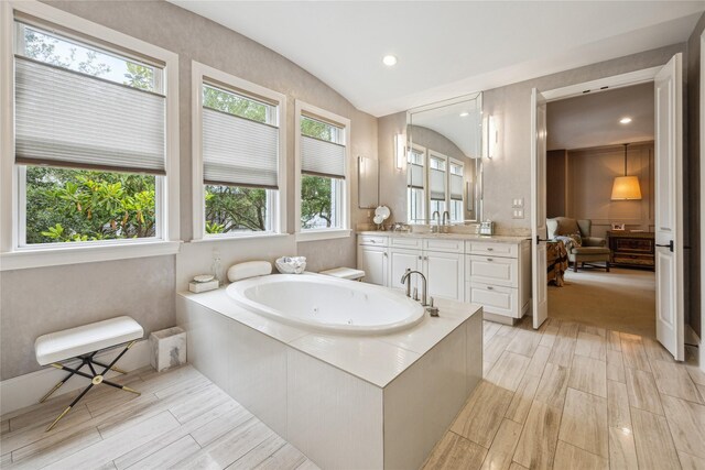 full bathroom with wood finished floors, vanity, a tub with jets, vaulted ceiling, and ensuite bath
