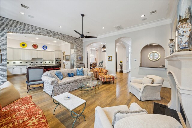 living area with arched walkways, ornamental molding, a ceiling fan, light wood-style flooring, and recessed lighting