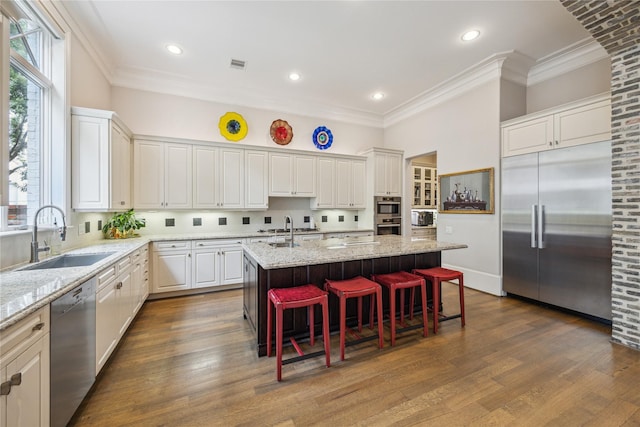 kitchen featuring appliances with stainless steel finishes, a sink, ornamental molding, an island with sink, and white cabinets