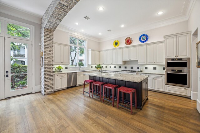 kitchen featuring appliances with stainless steel finishes, a sink, an island with sink, wood finished floors, and ornamental molding