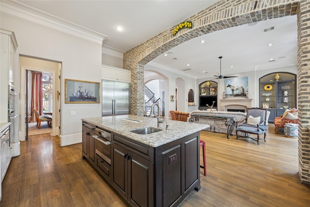 kitchen featuring stainless steel appliances, a sink, a fireplace, ceiling fan, and dark wood-style flooring