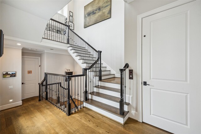 stairs featuring wood finished floors, baseboards, recessed lighting, ornamental molding, and a high ceiling
