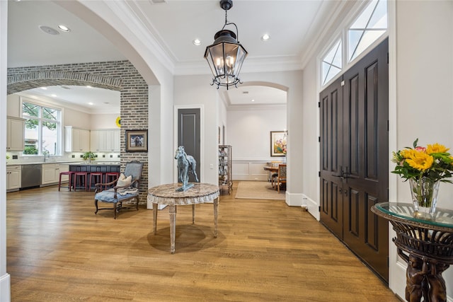 foyer entrance with arched walkways, light wood-type flooring, ornamental molding, and a chandelier