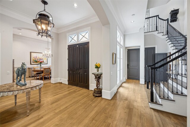 entryway featuring light wood finished floors, stairs, healthy amount of natural light, a chandelier, and ornamental molding