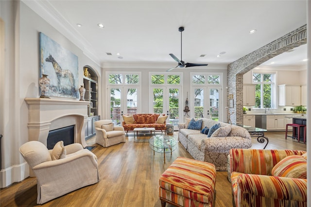 living area with ceiling fan, ornamental molding, light wood finished floors, recessed lighting, and a glass covered fireplace