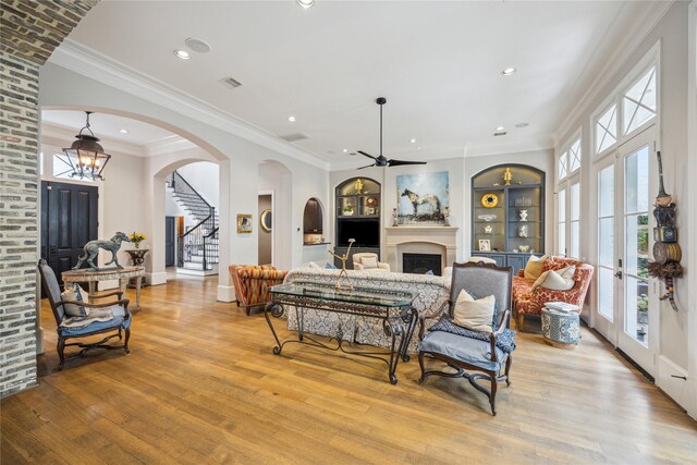 living area featuring arched walkways, light wood-type flooring, a fireplace, stairway, and ornamental molding