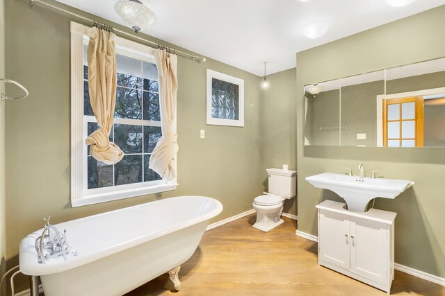 full bathroom featuring wood finished floors, a soaking tub, baseboards, a sink, and toilet