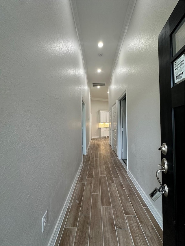 hall featuring ornamental molding, dark wood-style flooring, baseboards, and a textured wall