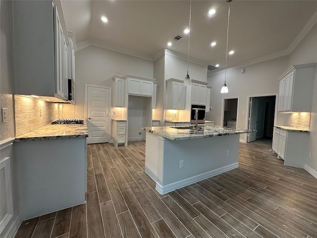 kitchen featuring crown molding, a sink, light stone counters, high vaulted ceiling, and a kitchen island with sink