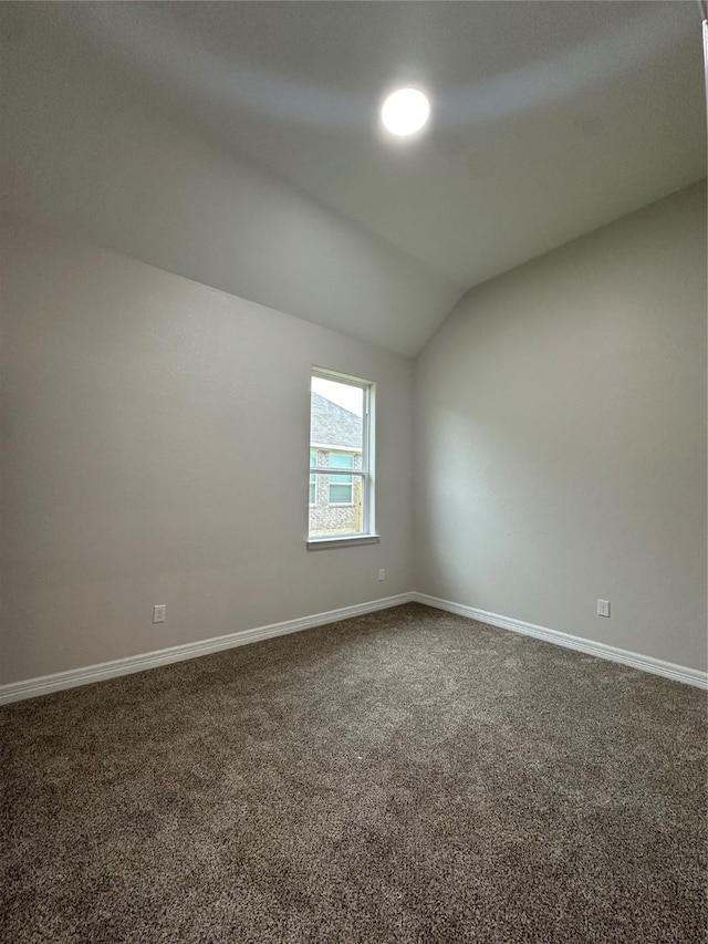 carpeted spare room featuring lofted ceiling and baseboards