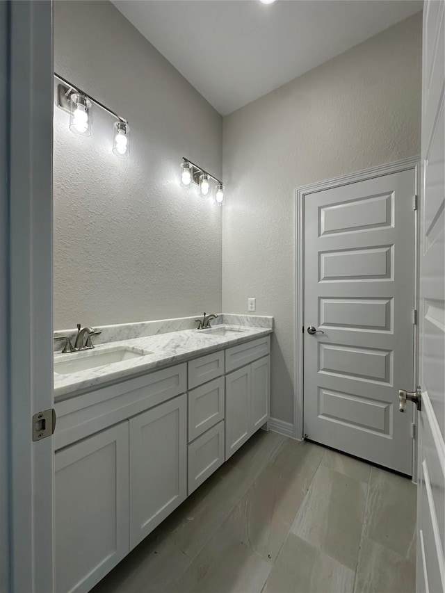 bathroom featuring double vanity, a textured wall, and baseboards