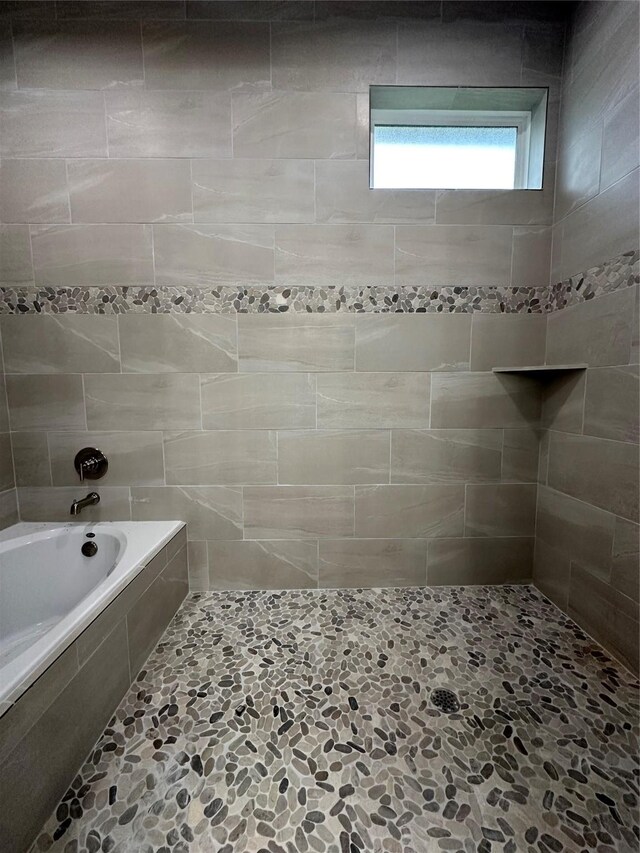 bathroom featuring a tile shower, tiled tub, and stone finish flooring