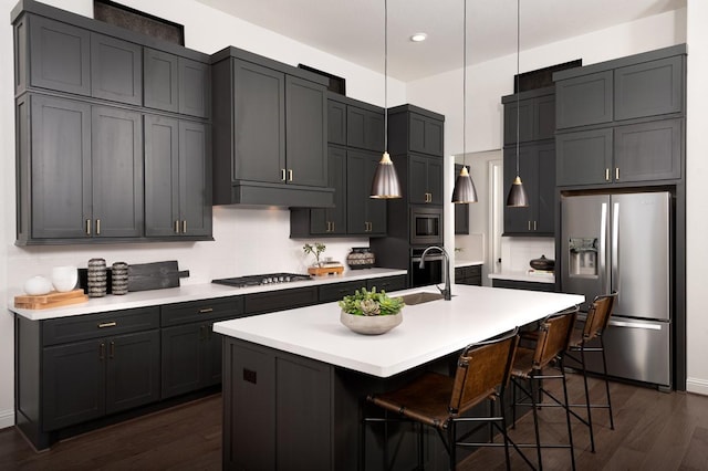 kitchen featuring appliances with stainless steel finishes, a sink, dark wood-style floors, light countertops, and pendant lighting
