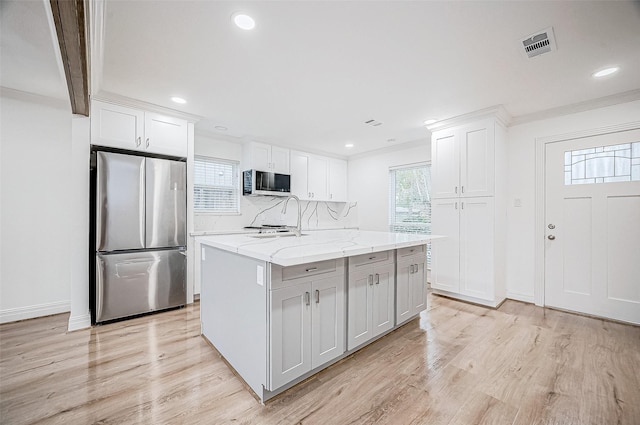 1739 Nocturne Ln, Houston, TX 77043 - kitchen with stainless steel appliances, light wood-style floors, white cabinets, a kitchen island with sink, and recessed lighting