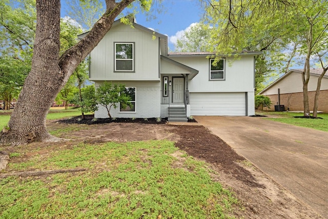 raised ranch featuring a garage, driveway, and brick siding