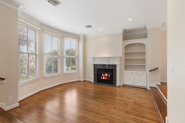 unfurnished living room featuring crown molding, a high end fireplace, wood finished floors, baseboards, and recessed lighting