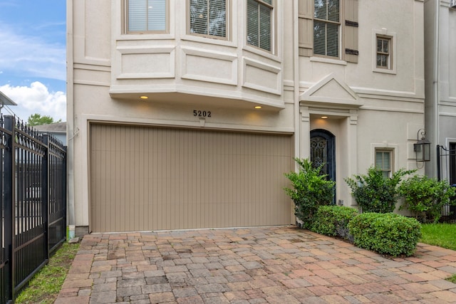 entrance to property featuring an attached garage, fence, stucco siding, and driveway