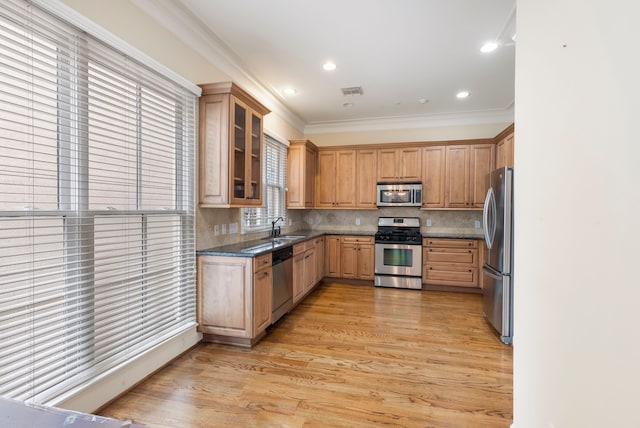 kitchen featuring stainless steel appliances, a sink, ornamental molding, light wood-style floors, and tasteful backsplash