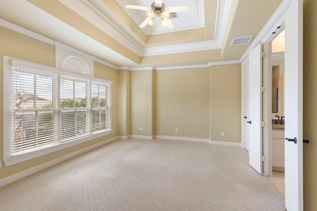 empty room with a raised ceiling, light colored carpet, a ceiling fan, crown molding, and baseboards